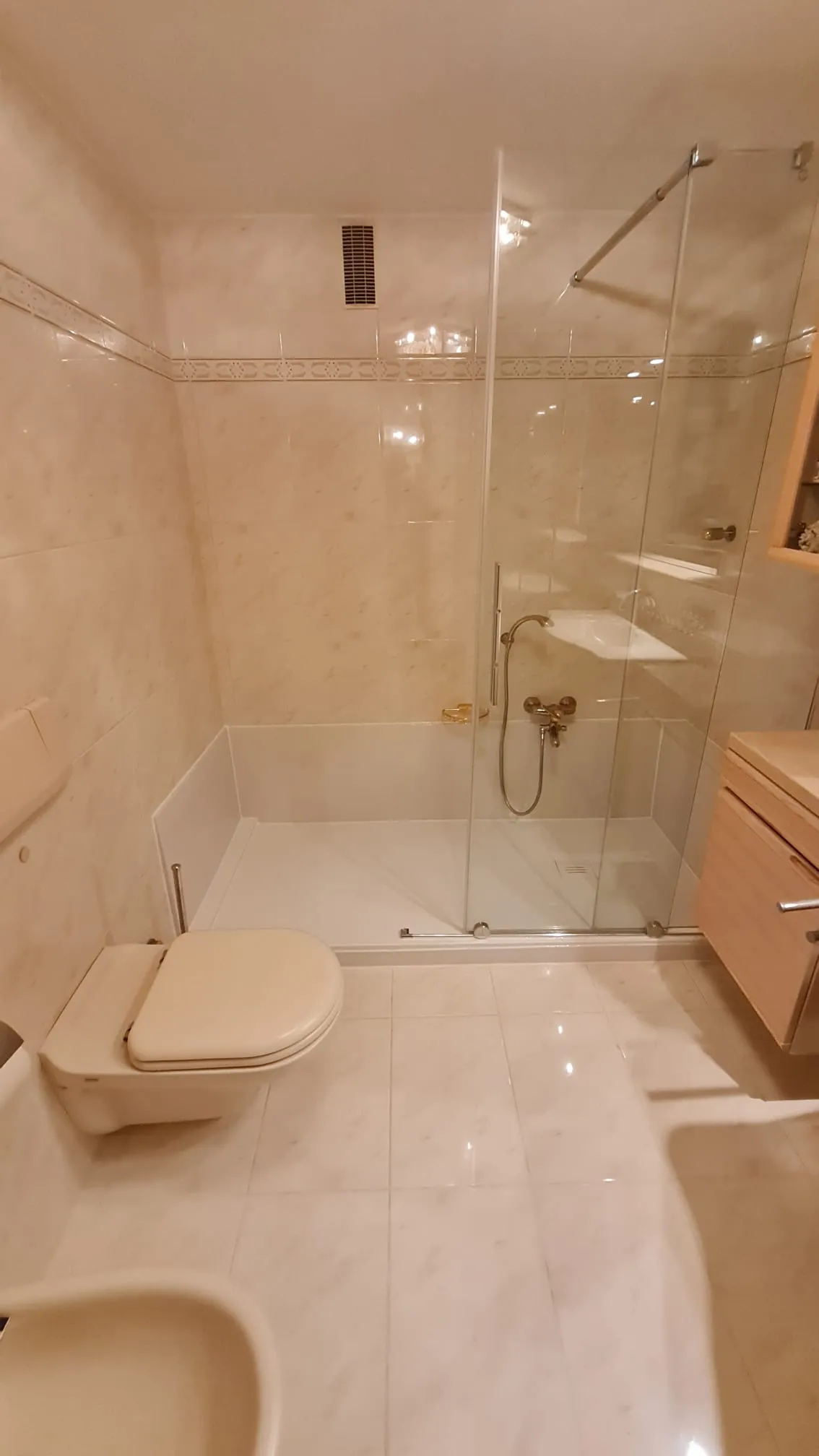 Bodengleiche Walk-in-Dusche mit Glaswand und hellen Fliesen in Marmoroptik