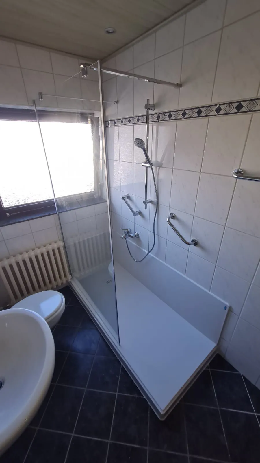 Neue Walk-in-Glasdusche mit dunklen Bodenfliesen nach dem Umbau von Badewanne zu Dusche
